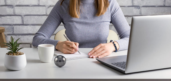 Woman writing on a notebook at a desk with EMF slider and laptop.